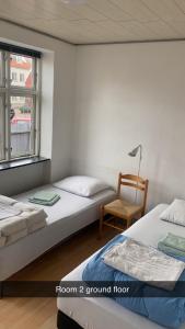 two beds in a room with a chair and a window at Byens Bed and Bath in Nakskov