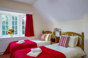 a bedroom with two beds with red sheets and a window at Benslow Music Historic Stay in Hitchin in Hitchin