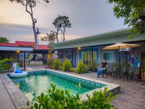 Eine Frau sitzt auf einem Stuhl an einem Swimmingpool vor einem Haus. in der Unterkunft Bunk Ubon Hostel in Ban Na Khwai