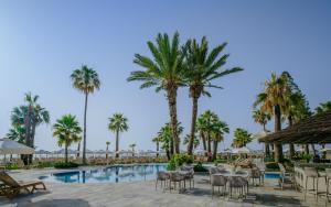 a resort pool with tables and chairs and palm trees at Golden Bay Beach Hotel in Larnaca