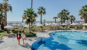 a couple walks by the pool at the resort at Golden Bay Beach Hotel in Larnaca