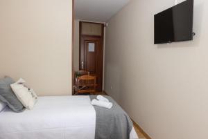 a bedroom with a white bed and a flat screen tv at Pensión A Codeseira Melide in Melide