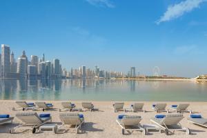 a row of chairs on a beach with a city at Dukes The Palm Dubai Hotel in Dubai