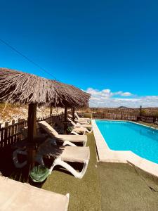 a swimming pool with lounge chairs and a straw umbrella at CASA RURAL PRIVADA El ASIENTO LOS GEMELOS in Pruna