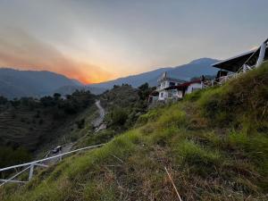 a house on a hill with the sunset in the background at Dhauladhar Eternals in Dharamshala