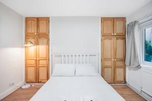 a bedroom with a white bed and wooden cabinets at Pass the Keys Private Garden Apartment by Tulse Hill Station in London