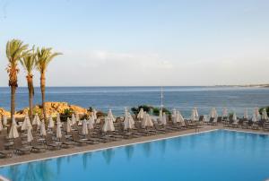 a swimming pool with lounge chairs and the ocean at Queens Bay Hotel in Paphos