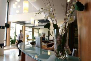 a vase with white flowers on a glass table at Brit Hotel du Lac in Saint-Paul-lès-Dax