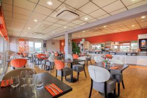 ein Restaurant mit Tischen und Stühlen und einer Küche in der Unterkunft Brit Hotel Les Evens in Saint-Saturnin