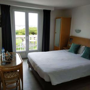 a bedroom with a bed and a table and a balcony at Brit Hotel Hermitage in Royan