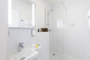 La salle de bains blanche est pourvue d'un lavabo et d'une douche. dans l'établissement Résidence Studio Genève Centre, à Genève