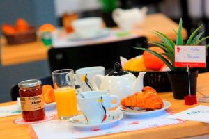 a table with a breakfast of orange juice and croissants at Brit Hotel Le Polder in Gravelines