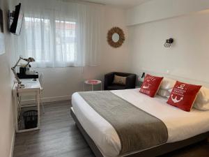 a bedroom with a bed with red pillows and a desk at Cit'Hotel Le Ch&ecirc;ne Vert in Les Sables-dʼOlonne