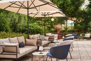une terrasse avec des canapés, des tables et un parasol dans l'établissement Hôtel Le Versailles, à Versailles
