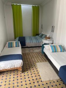 two beds in a room with green curtains at Riad Aicha in Asilah