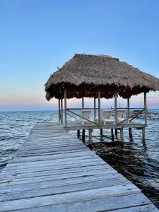 a wooden pier with a straw umbrella and the ocean at Barefoot Beach Belize in Caye Caulker