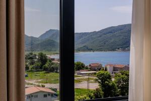 a window with a view of a lake and mountains at Hotel AQUILO in Petrovac na Moru