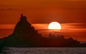 a sunset with a lighthouse on a rock in the ocean at Hotel AQUILO in Petrovac na Moru