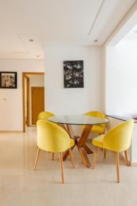 a dining room with a glass table and yellow chairs at New Luxurious apartment Agdal Rabat center in Rabat +12 photos