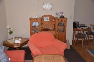 a living room with an orange chair and a wooden cabinet at Ferienwohnung Krummhörn Upleward in Krummhörn