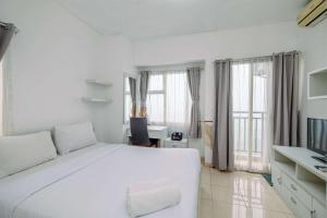 a white bedroom with a large white bed and windows at Simple and Cozy Living Studio Apartment at Margonda Residence 3 By Travelio in Depok +4 photos