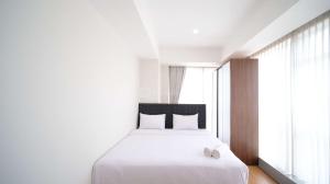 a bedroom with a white bed and a large window at Simple and Clean 2BR at Grand Sungkono Lagoon Apartment By Travelio in Surabaya +19 photos