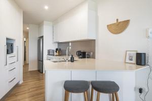a kitchen with white cabinets and two stools at Tranquil Tides Retreat - Coastal Waterfront Escape in Caloundra