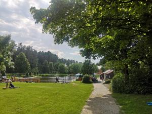 a park with people sitting on the grass next to a river at Die Badeanstalt I Loft Nürnberg I 5 Minuten zu Fuß zum kostenlosen Naturbad I Messenähe I Waldnähe in Postbauer-Heng