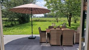 a wooden table with chairs and an umbrella at Huisje Weidezicht in Lievelde