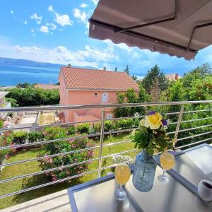 une table avec deux verres et un vase de fleurs sur un balcon dans l'établissement LIGHTHOUSE, à Novi Vinodolski