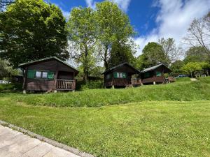three cottages on a grassy hill with trees at Camping de Tauves in Tauves