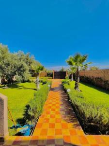 Un camino de baldosas amarillas con palmeras y un campo. en Villa1 des tortues Marrakech, en Aït Zat