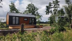a tiny house with a black roof in a field at TinyHouse Ochtendgloren in Haastrecht +6 photos
