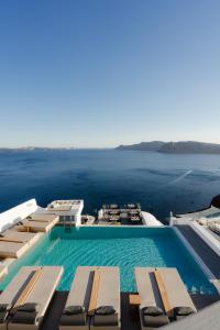a pool with chairs and the ocean in the background at La Perla Villas and Suites - Adults Only in Oia