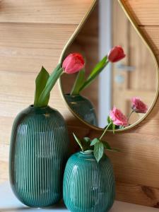 two green vases with flowers in them in front of a mirror at Hygge Lodge Annecy in Doussard