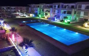 a swimming pool at night with palm trees and buildings at Malaga Beach El Mansouria in Mansouria