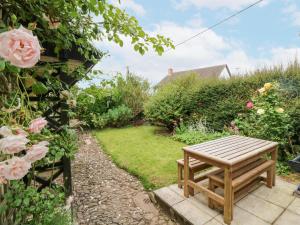 een houten bank in een tuin met rozen bij Westgate Cottage in Lapford