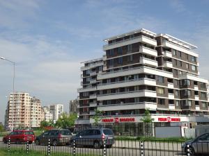 Un grand bâtiment avec des voitures garées devant lui dans l'établissement Mladost Apartments Sofia, à Sofia