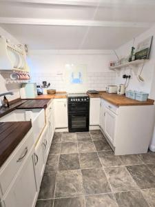 - une cuisine avec des placards blancs et une cuisinière noire dans l'établissement Lobster Pot Cottage, à Fulmodeston 9 autres photos