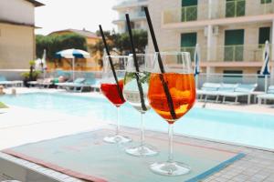 two wine glasses sitting on a table near a swimming pool at Hotel Bristol in Caorle