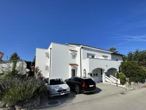 two cars parked in front of a white house at Guest House Šulek in Punat
