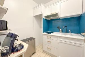 a small kitchen with white cabinets and blue walls at Flexliving - room - Hillairet in Paris