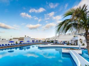 a swimming pool with a palm tree and chairs at BelleVue Aquarius in Puerto del Carmen