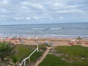 a beach with people and umbrellas and the ocean at Maison d'hôte sur la Plage de Bouznika in Bouznika