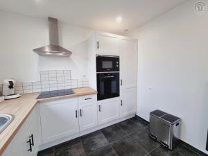 une cuisine avec des armoires blanches et des appareils noirs dans l'établissement Gîte de Charme avec Jardin Privé, Proche de Lille et Hazebrouck, Idéal pour Familles et Cyclistes - FR-1-510-209, à Haverskerque