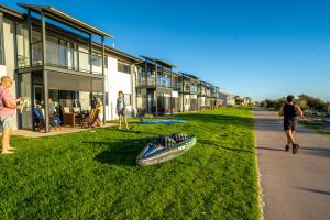 Port AdelaideBeach Stayz Semaphore Three Bedroom Apartment的一条船躺在建筑物旁边的草上