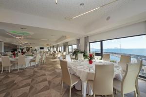 una sala da pranzo con tavoli e sedie bianchi e grandi finestre di Hotel Poseidon a Torre del Greco