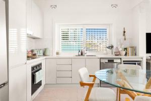 a kitchen with white cabinets and a glass table at Beachside Boho Retreat by Sydney Dreams in Sydney +27 photos