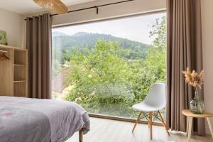 Un dormitorio con una gran ventana y una silla blanca. en Gîte exceptionnel a Soultzbach les bains, en Soultzbach-les-Bains