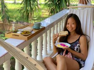 Una mujer sentada en un porche sosteniendo un sándwich y un plato de comida. en MY HOME Resort - Koh phangan vacation house rentals, en Ban Madua Wan